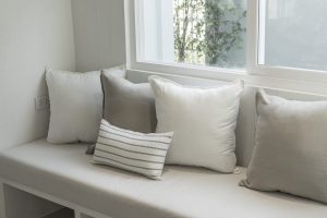 Corner of stylish living room with white walls, wooden floor, comfortable gray sofa with cushions near window
